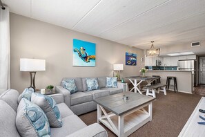 A living room with a sofa, coffee table, and a kitchen area in the background.