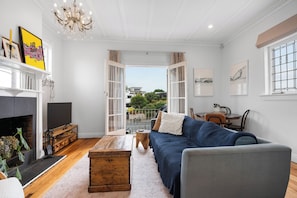 A spacious living room with a fireplace, a blue sofa, a wooden coffee table, and a chandelier. - Character 1 BDR 1920s apartment Mount Eden Village (Auckland)