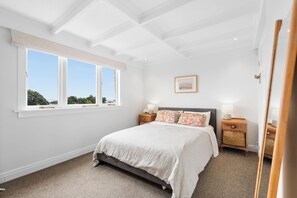 Une chambre avec un grand lit, deux tables de chevet, une fenêtre donnant sur un beau paysage et un tableau encadré au mur.