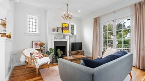 Una sala de estar con chimenea, un sofá, un televisor y un amplio ventanal con cortinas.