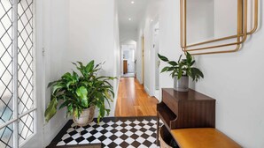 Un pasillo con suelo a cuadros, un banco de madera, dos plantas en macetas y un espejo en la pared.