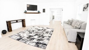 A modern living room with a large black and white rug, a grey sofa, a wooden bench, and a TV mounted on the wall. -     Cozy Atlanta Stay Sleeps 4 Near ATL. Free Wifi + Self check in (College Park)