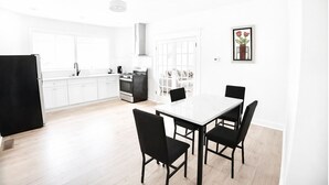 A modern kitchen with white cabinets, a black refrigerator, and a dining area with a white table and black chairs. -     Cozy Atlanta Stay Sleeps 4 Near ATL. Free Wifi + Self check in (College Park)