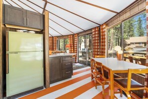 A kitchen with a refrigerator, cabinets, and a dining area with a table and chairs. - Carousel House - Retro 70's Home - SHARC (Sunriver)