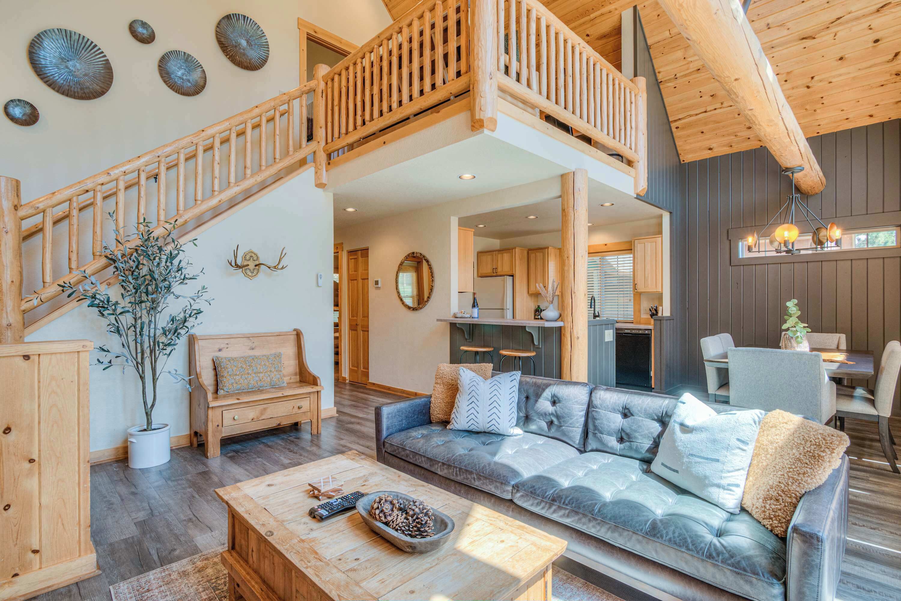 A spacious living area with a wooden staircase, a sofa set, a dining area, and a kitchen.