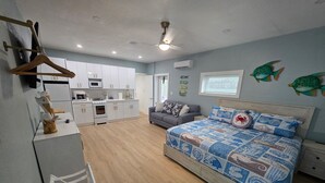 Una camera da letto con un letto, un divano grigio, un pavimento in legno, un armadio bianco e un angolo cottura con mobili bianchi e un forno a microonde.
