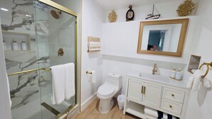 Un bagno moderno con cabina doccia in vetro, un water bianco e un mobile lavabo con dettagli dorati.