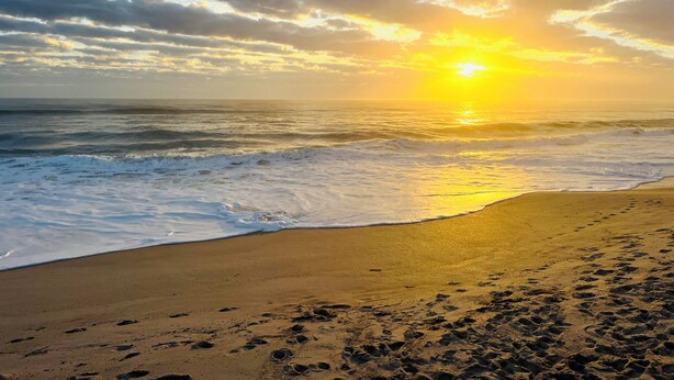 Una spiaggia con impronte che conducono all'acqua, un tramonto e un cielo nuvoloso.