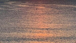 Tramonto sull'oceano con una persona in piedi sulla spiaggia.