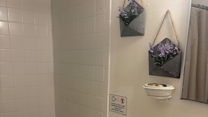 A bathroom with white tiles, a toilet, a sink with a mirror, a shower curtain rod, and a sign prohibiting flushing feminine products. - Small studio (West Palm Beach)