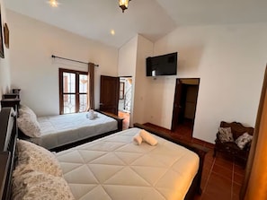 Ein Schlafzimmer mit zwei Betten, einem Fernseher und einem Fenster mit Vorhängen.