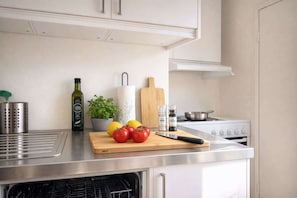 A kitchen with a stainless steel countertop, a cutting board with tomatoes, lemons, and a knife, a potted plant, a bottle of olive oil, a paper towel holder, and a stove. - 4 Bedrooms, King Bed, in the Heart of Bergen (Bergen)