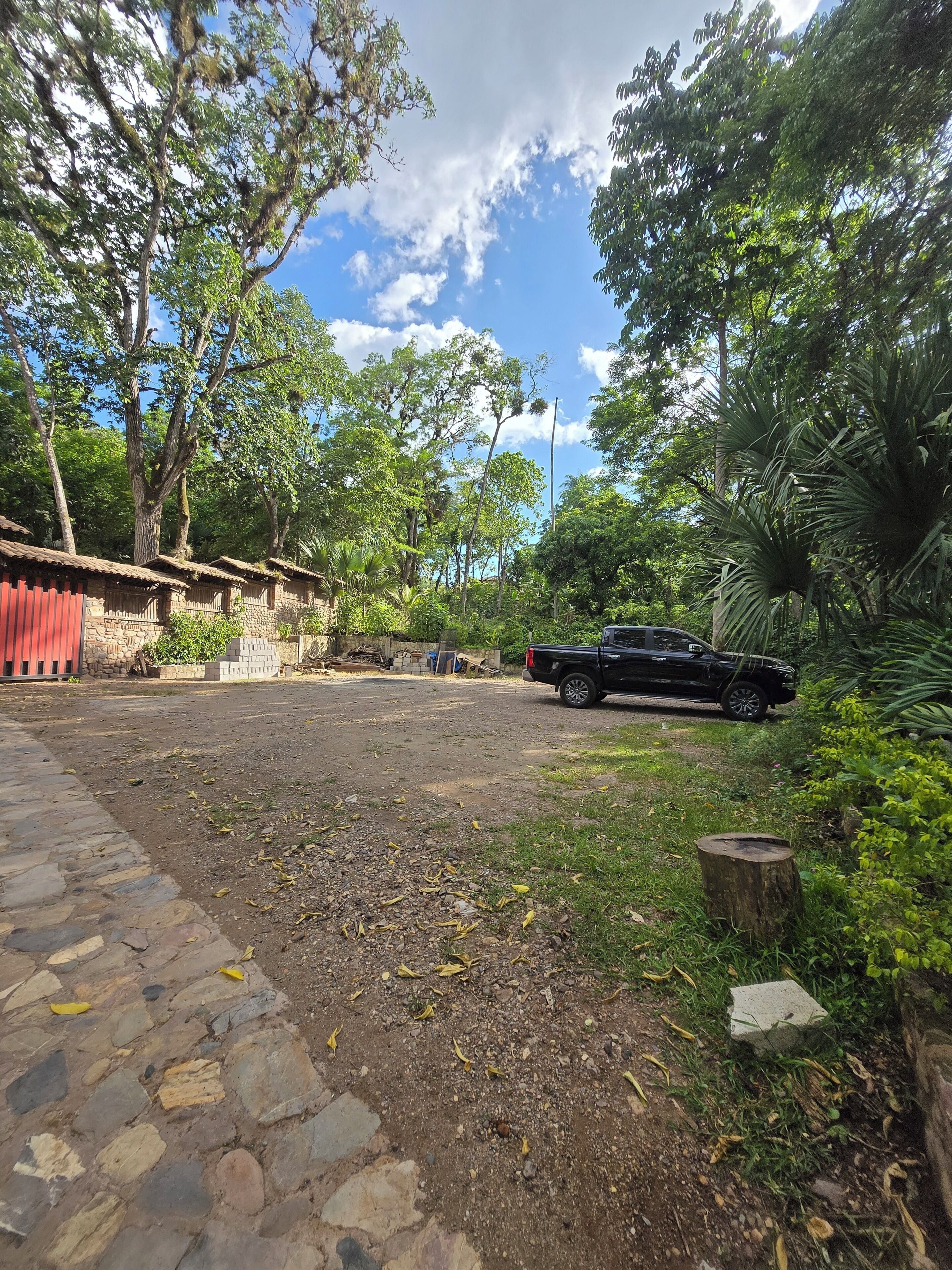Una zona pavimentada con borde de piedra, un vehículo negro y un edificio rojo al fondo.