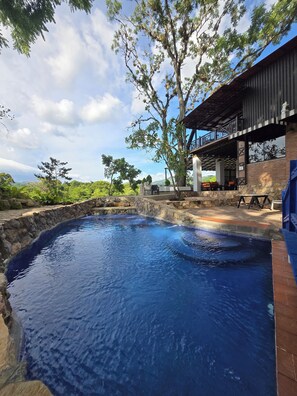 Ein Pool mit Steinwänden, ein überdachter Sitzbereich im Freien und Blick auf die umliegende Landschaft.