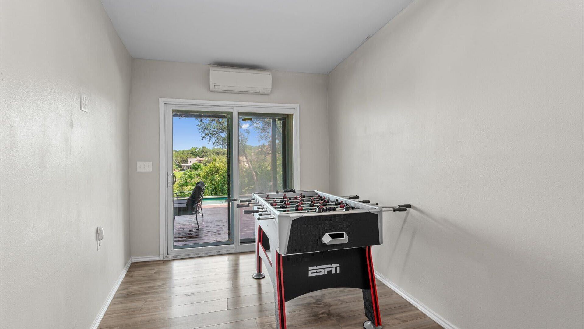 Een kamer met een tafelvoetbaltafel, een schuifdeur naar een terras en een airconditioning in het plafond.