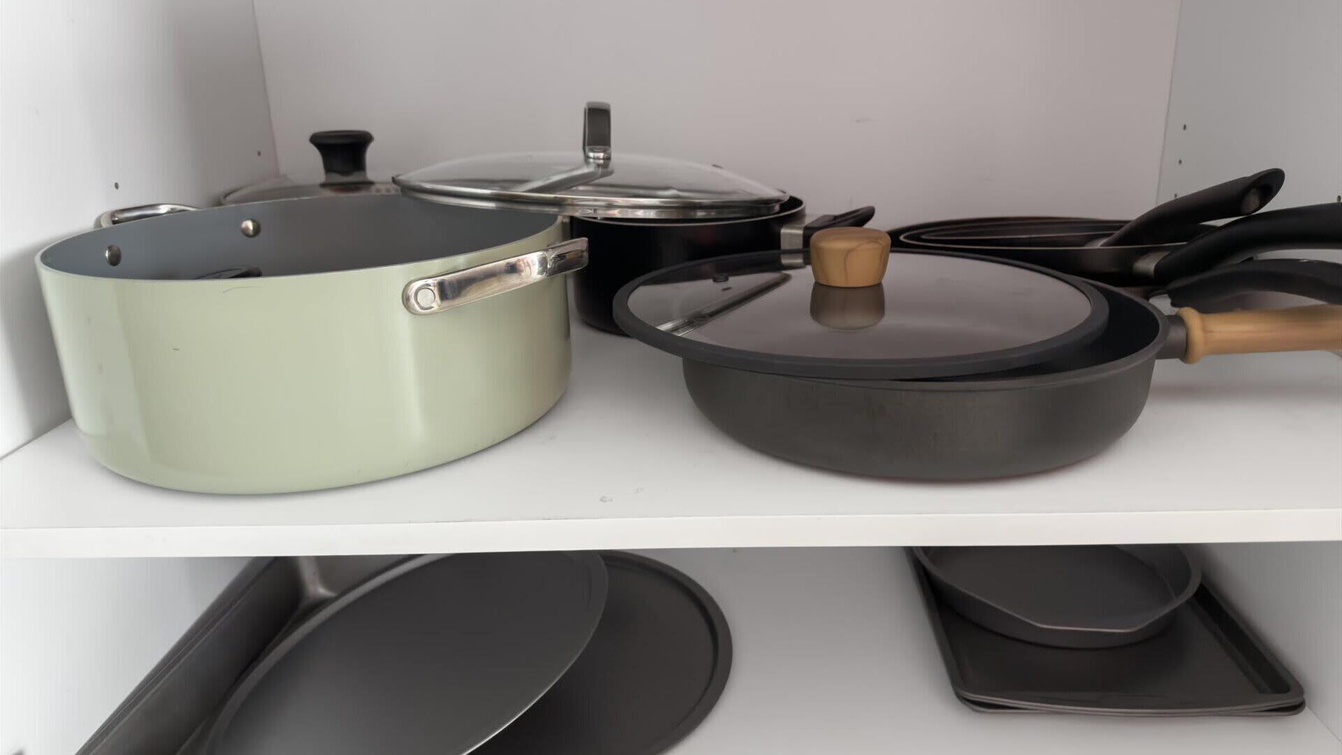 A kitchen shelf with various cookware including a green pot, a black pan, and a frying pan with wooden handles.