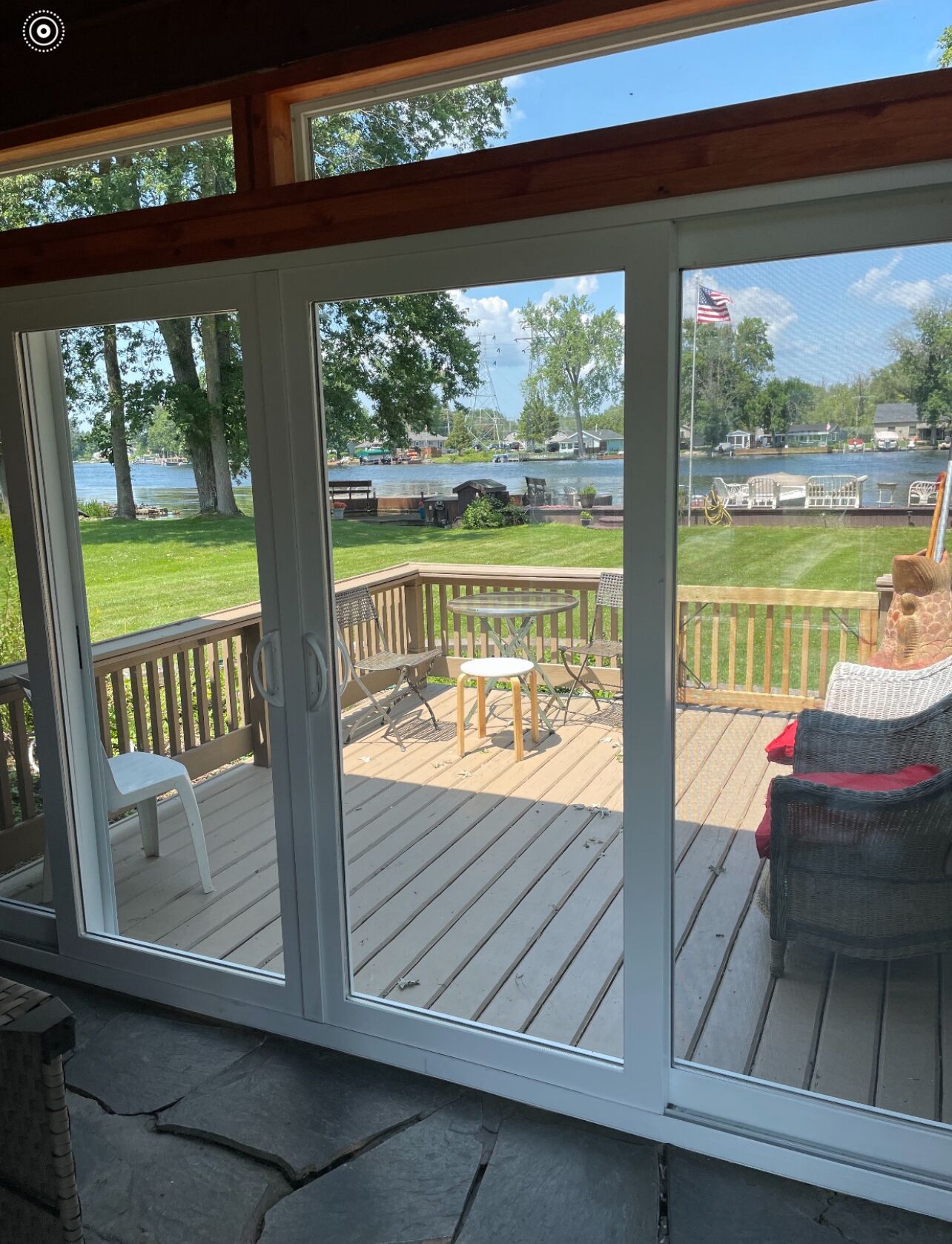 A covered deck with a view of a lake, outdoor furniture, and an American flag.