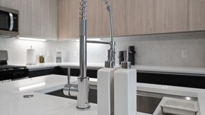 A modern kitchen with a stainless steel faucet, a microwave, and a sink. - Upstay: Modern & Pet-friendly 2BR Home Near Soco (Austin)