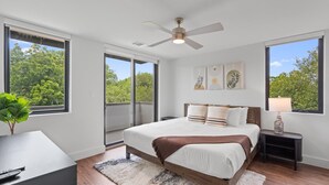 Une chambre à coucher comprenant un lit, une table de chevet, un bureau, un ventilateur de plafond et de grandes fenêtres.