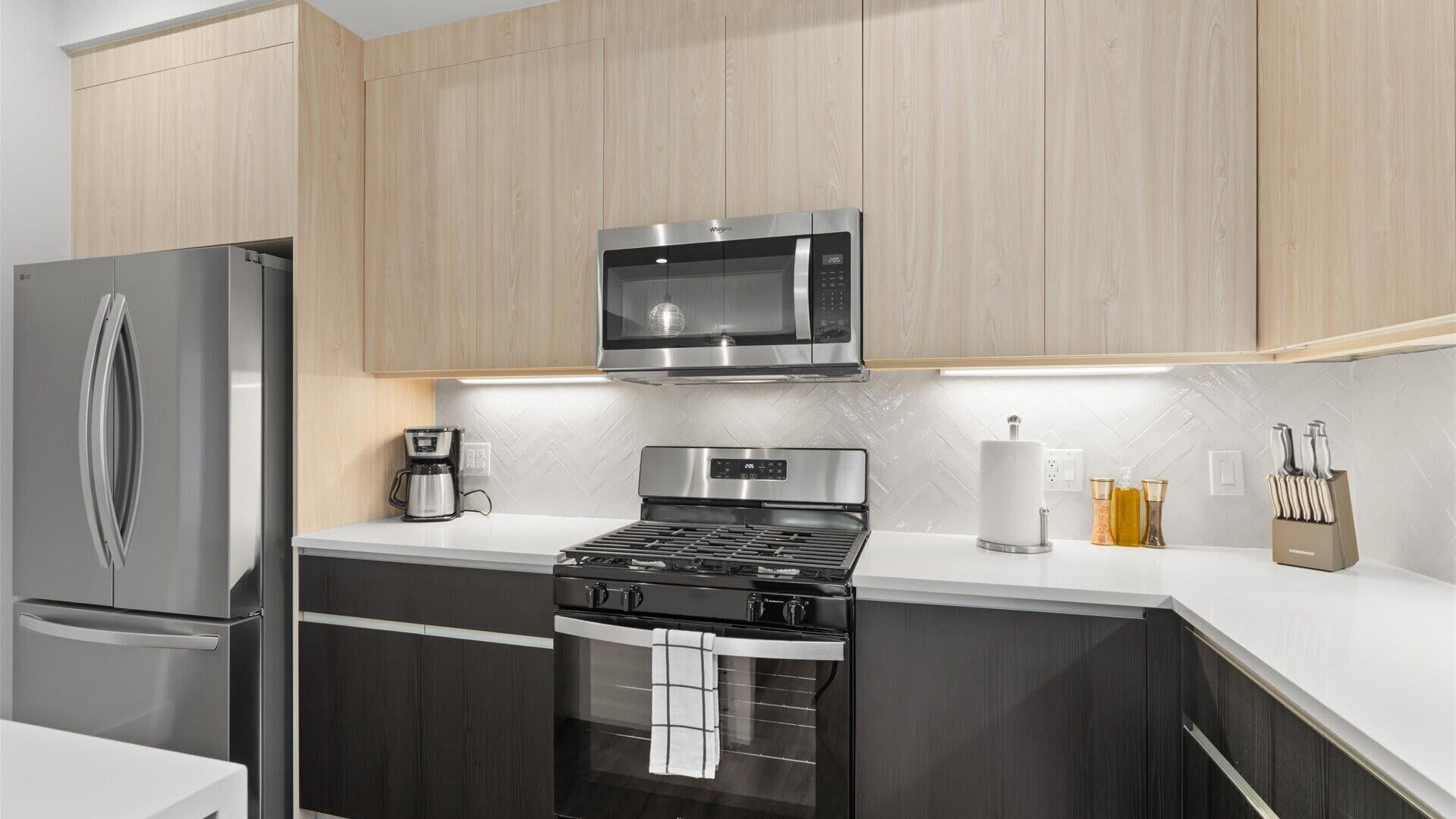 A modern kitchen with stainless steel appliances, wooden cabinets, and a white countertop.