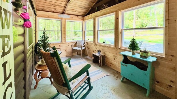 A cozy cabin interior with wooden walls, a rocking chair, a small table, and a window overlooking greenery. - 20 Mins To Hershey Park w/ Farm Animals & Firepit! (Grantville)