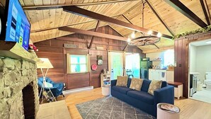 A cozy cabin interior with a stone fireplace, a blue sofa, a rug, and a TV mounted on the wall. - 20 Mins To Hershey Park w/ Farm Animals & Firepit! (Grantville)