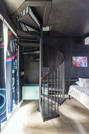 Een kleine kamer met een wenteltrap, een bed, een klein kastje en een tv aan de muur.