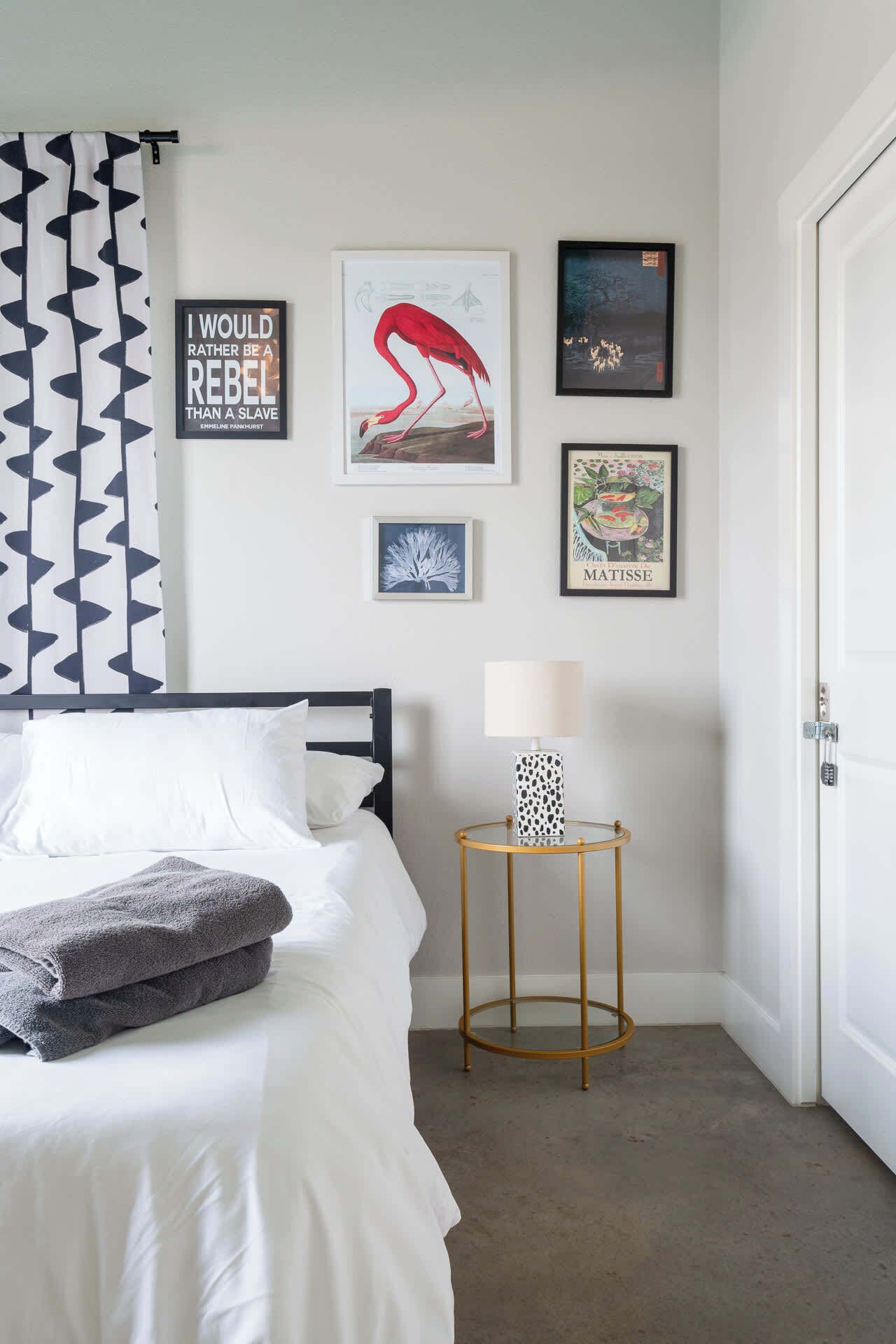 Quarto com cama, mesa de cabeceira e abajur, e decoração de parede incluindo uma frase inspiradora e uma ilustração de flamingo.