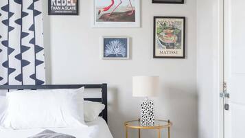 A bedroom with a bed, a nightstand with a lamp, and wall art including a quote and a flamingo illustration.