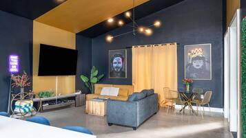 Una sala moderna con un sofá, televisor, comedor con sillas y obras de arte en las paredes.