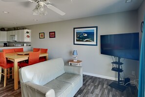 Un salon comprenant un canapé, une table à manger avec des chaises, un téléviseur et un ventilateur de plafond.