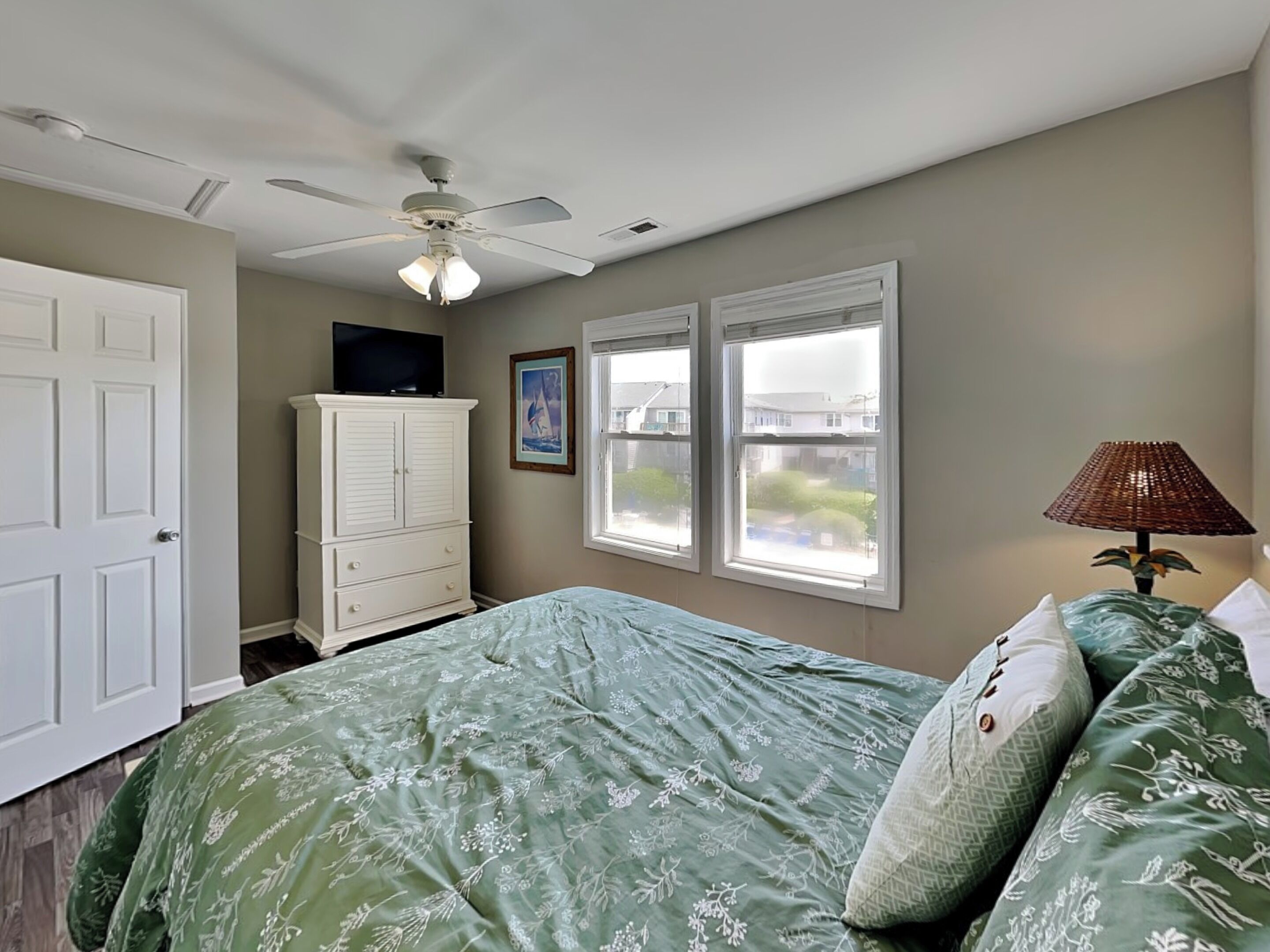 Une chambre à coucher avec un lit, un ventilateur de plafond, une commode, un téléviseur et des fenêtres.