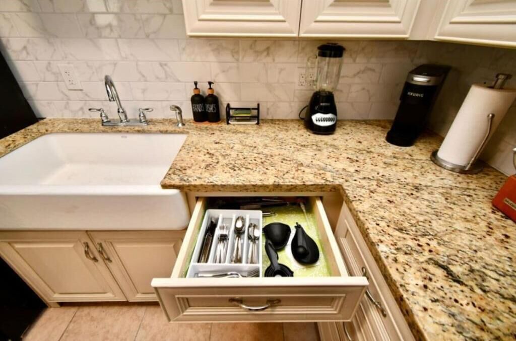 Una cocina con encimera de granito, un lavabo y un organizador de cajones con utensilios.