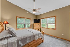 A bedroom with a bed, a TV, a ceiling fan, and two windows with blinds.
