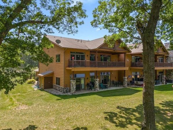 A two-story lodge with a balcony on the second floor, a covered patio, and a stone foundation.