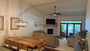 Amplia sala de estar con chimenea, zona de comedor con mesa y sillas de madera, sofá y televisor montado en una pared de piedra.