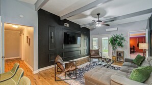 Un salon avec un mur de couleur sombre, un ventilateur de plafond, un téléviseur à écran plat, une cheminée et une plante verte.