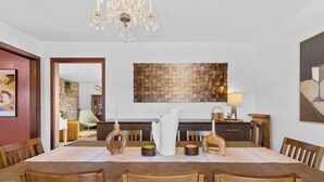 A dining room with a wooden table, chairs, a chandelier, and a wall art piece.