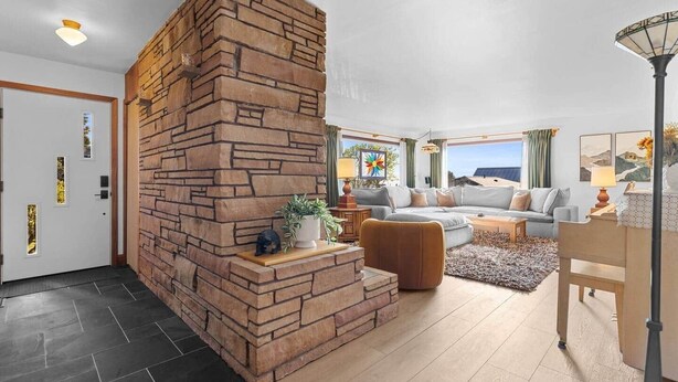 A modern living room with a stone fireplace, a sectional sofa, a coffee table, and a lamp.