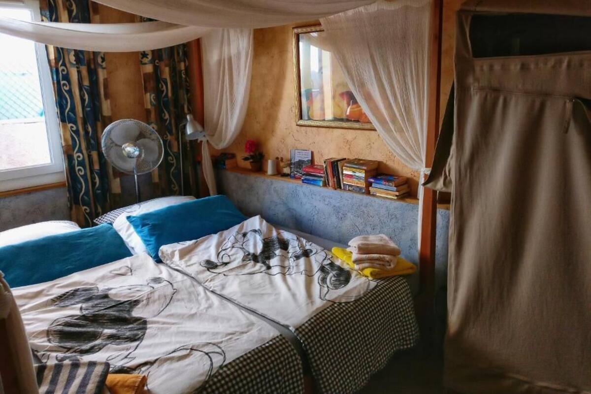 A bedroom with a bed, a bedside table, a window, and a fan.
