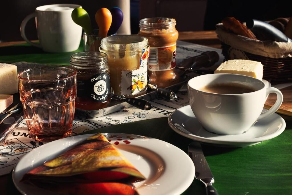 A breakfast setting with a cup of coffee, a glass of tea, a plate with toast, and jars of spreads.