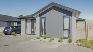 Ein modernes, zweigeschossiges Haus mit Garage, einem Auto auf der Auffahrt und einem kleinen Garten mit Sträuchern.