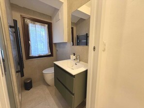 A bathroom with a toilet, sink, and window.