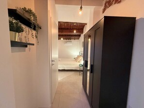 A narrow hallway leading to a bedroom with a bed, a small table, and a wall-mounted air conditioner.