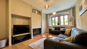 Una sala de estar moderna con un televisor de pantalla plana, un sofá, una mesa de centro y un amplio ventanal con cortinas.