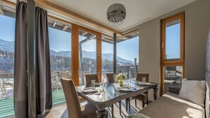 Un comedor con una mesa dispuesta para cuatro personas, ventanas amplias y vistas a las montañas.
