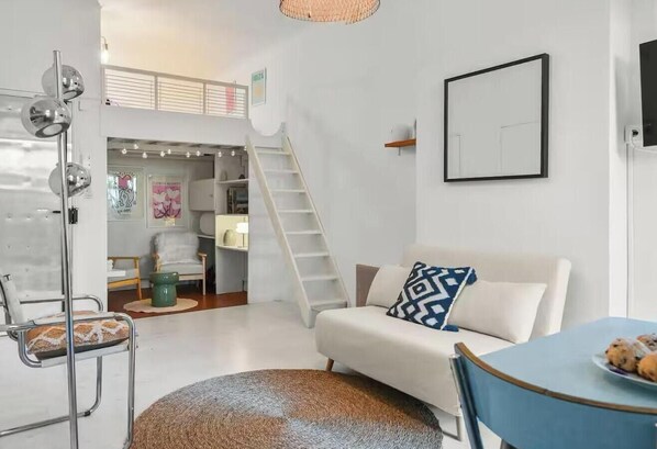 Una sala de estar moderna con un sofá, una mesa de centro, una silla, una escalera y un espejo montado en la pared.