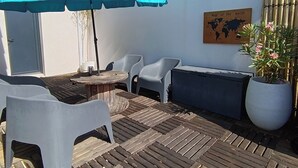 An outdoor patio with a wooden deck, a round table, two white plastic chairs, a blue umbrella, and a potted plant. - Family home with private heated pool and air conditioning (Biscarrosse)