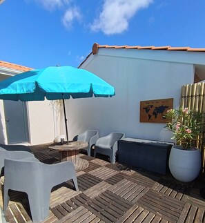 An outdoor patio with a wooden deck, a round table, two white plastic chairs, a blue umbrella, and a potted plant. - Family home with private heated pool and air conditioning (Biscarrosse)