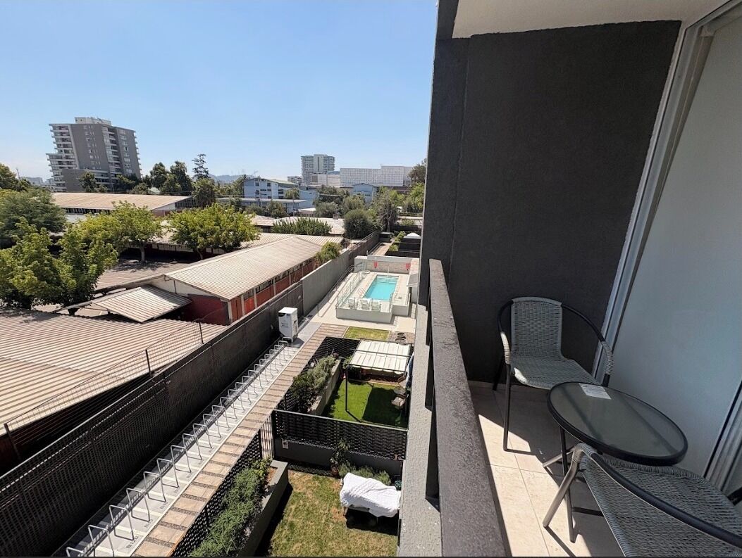A balcony with a view of a swimming pool, a fenced garden, and surrounding buildings.